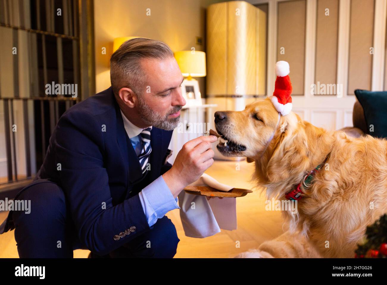 NUR FÜR REDAKTIONELLE VERWENDUNG Butler Lucas Kongiel hilft Golden Retriever Boris bei der Kostprobe von Hiltons neuem festlichen Menü für Hunde im Biltmore Mayfair, LXR Hotels & Resorts, London. Ausgabedatum: Dienstag, 23. November 2021. Stockfoto