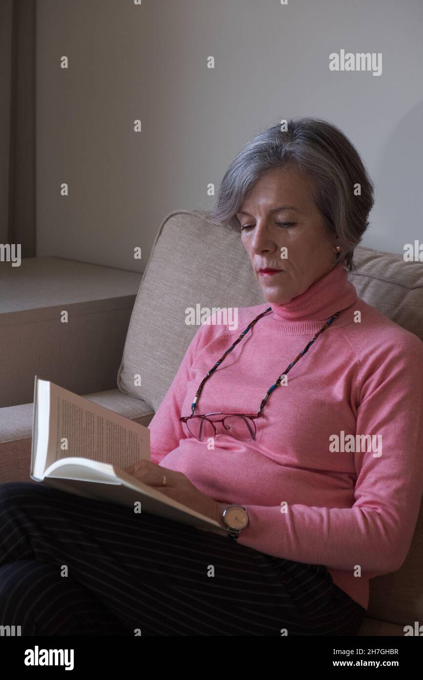 Ältere Frau in einer Brille, die sich auf dem Sofa ausruht und ein Buch liest. Konzept Hobby. Stockfoto