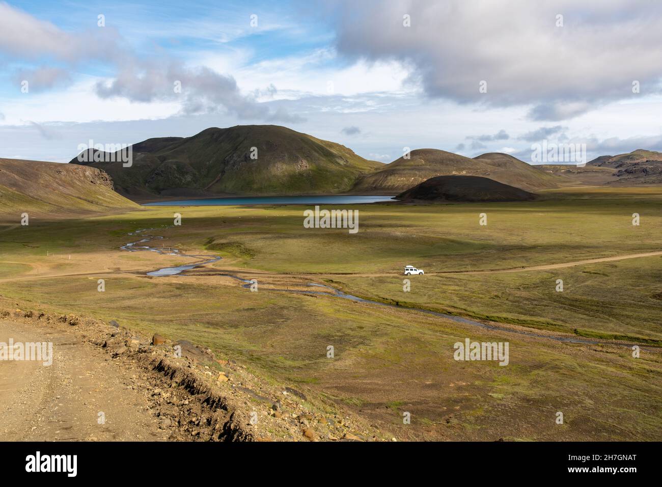 Hochwinkel-Panoramablick über das Hochplateau mit See und Feldweg und Allradfahrzeug in der Nähe des Katla Vulkans in Island mit Bergen im Hintergrund Stockfoto