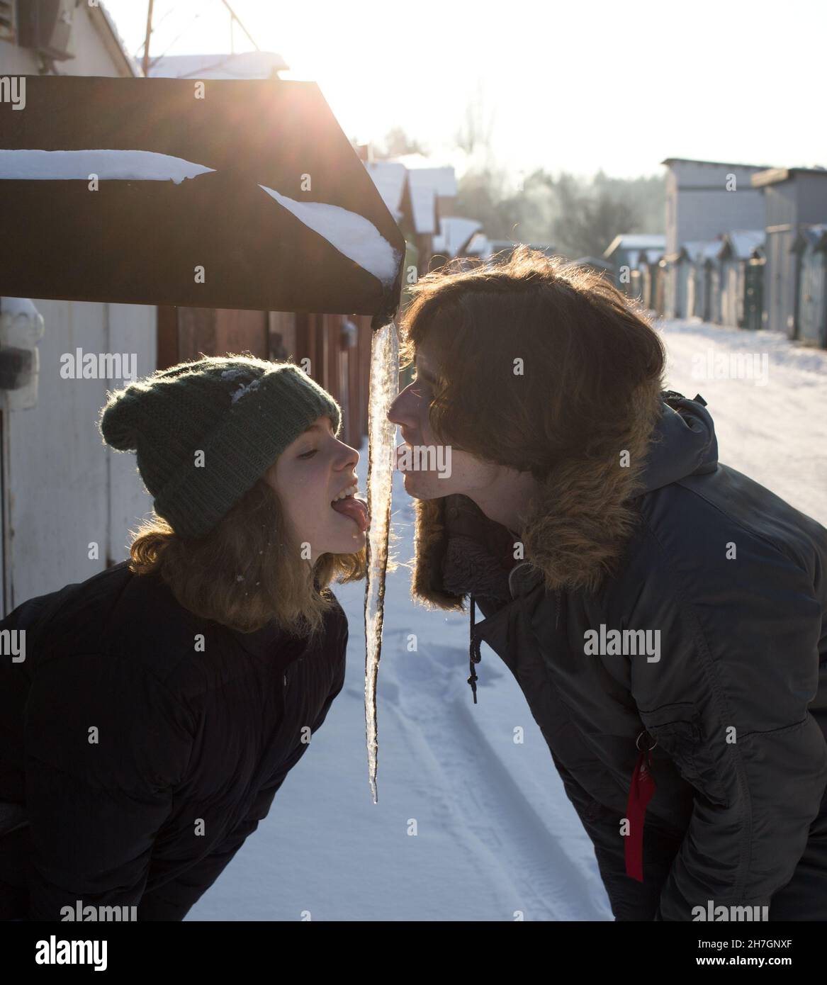 Fröhliches Teenager-Mädchen und Junge, etwa 16-17 Jahre alt, lecken ein großes Eiszapfen mit ihren Zungen. Viel Spaß und schauen sich gegenseitig an. Gutes Beziehungskonzept, Stockfoto