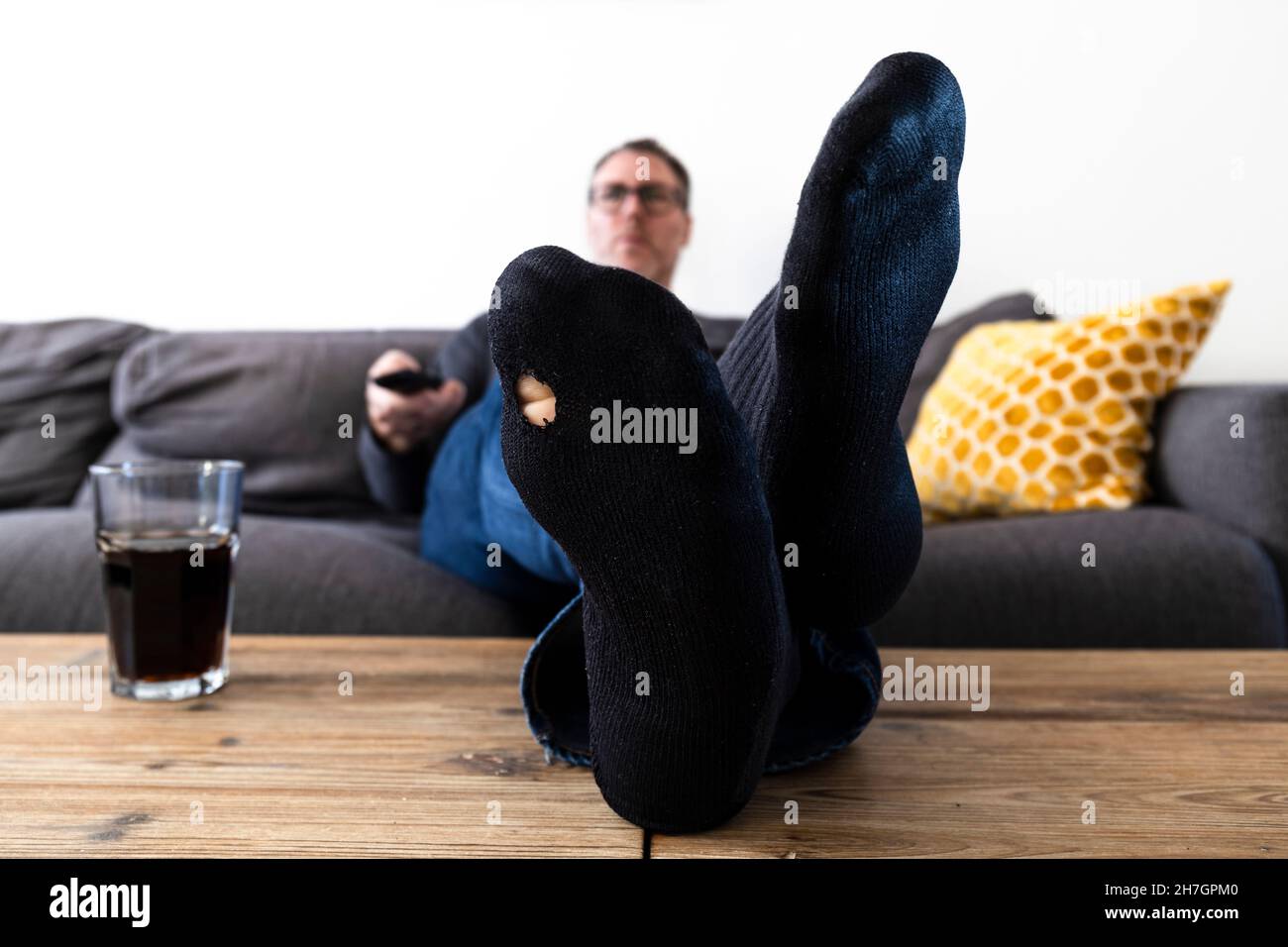 Erwachsener Mann mit einem Loch in seiner Socke, der Fernsehen schaute und die Fernbedienung benutzte Stockfoto