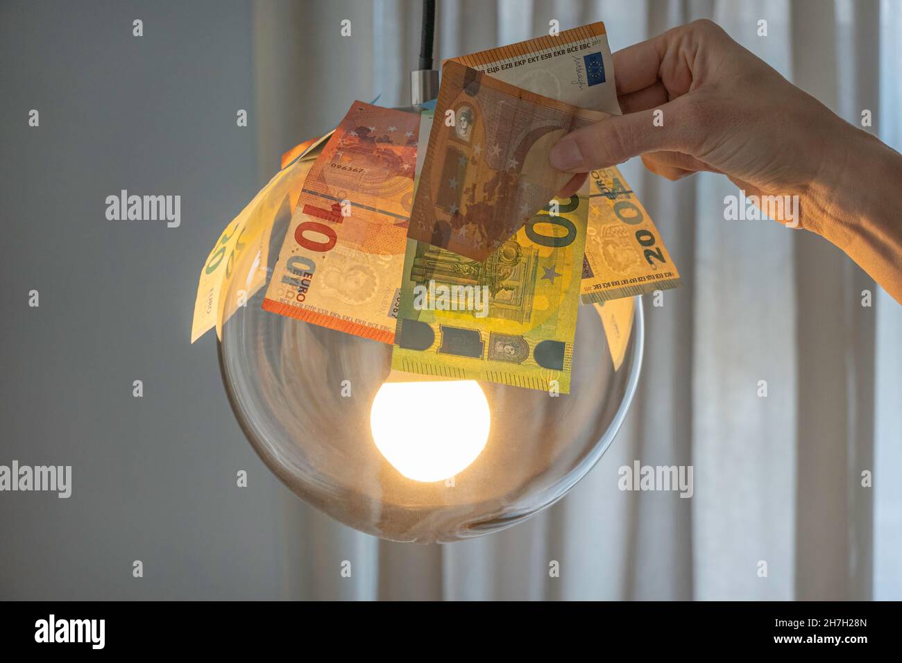 Euro-Scheine über glühender Lampe und eine Frau, die die Euro-Banknote hält. Stromkosten, Stromrechnung Zahlung, teure Energie-Konzept Stockfoto
