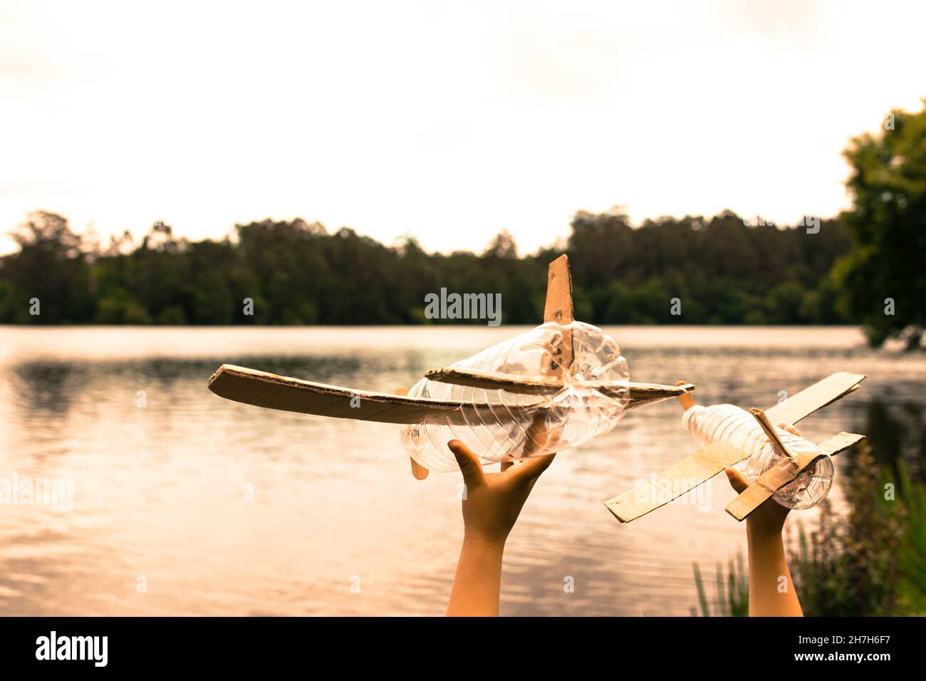 Kinderhände spielen mit einem Flugzeug aus recyceltem Material (Holz, PVC-Flaschen, Pappe) Stockfoto
