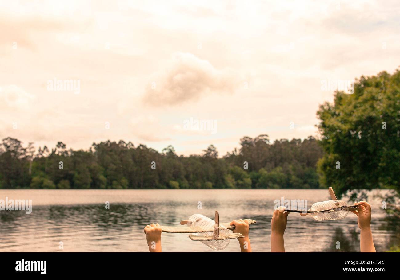 Kinderhände spielen mit einem Flugzeug aus recyceltem Material (Holz, PVC-Flaschen, Pappe) Stockfoto
