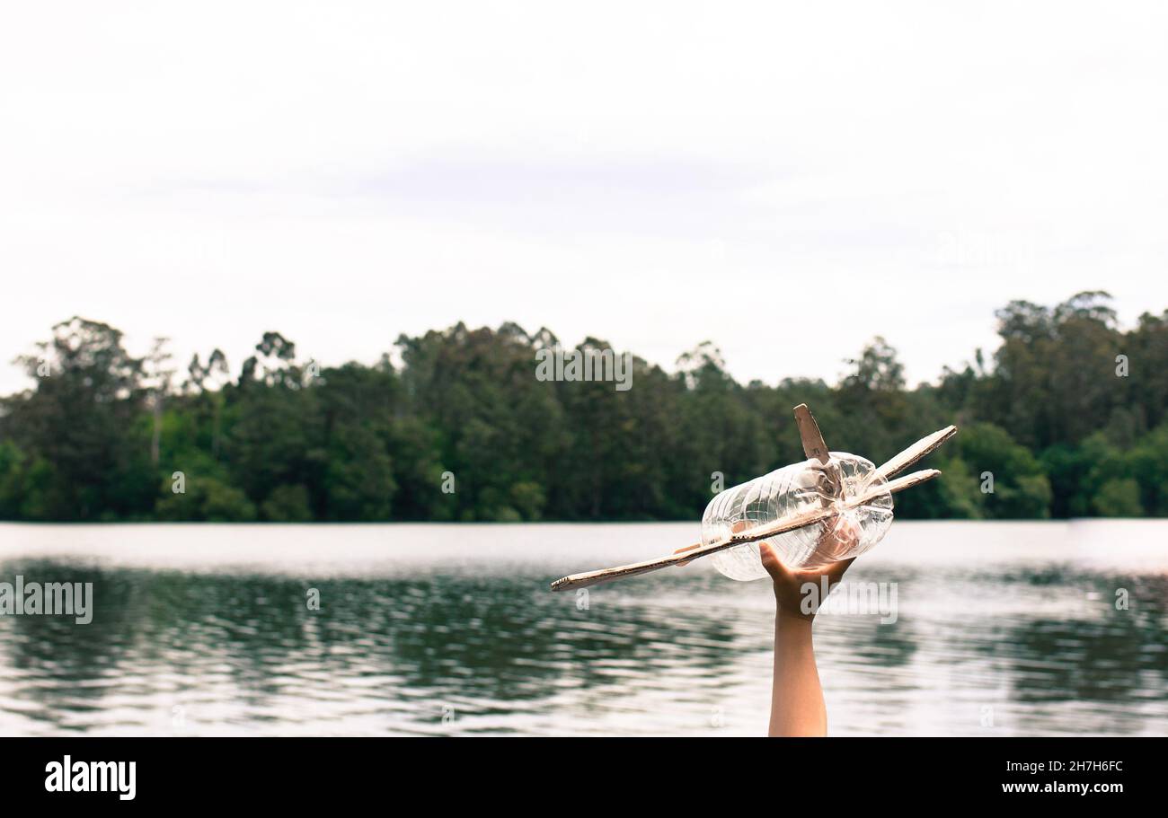 Kinderhände spielen mit einem Flugzeug aus recyceltem Material (Holz, PVC-Flaschen, Pappe) Stockfoto
