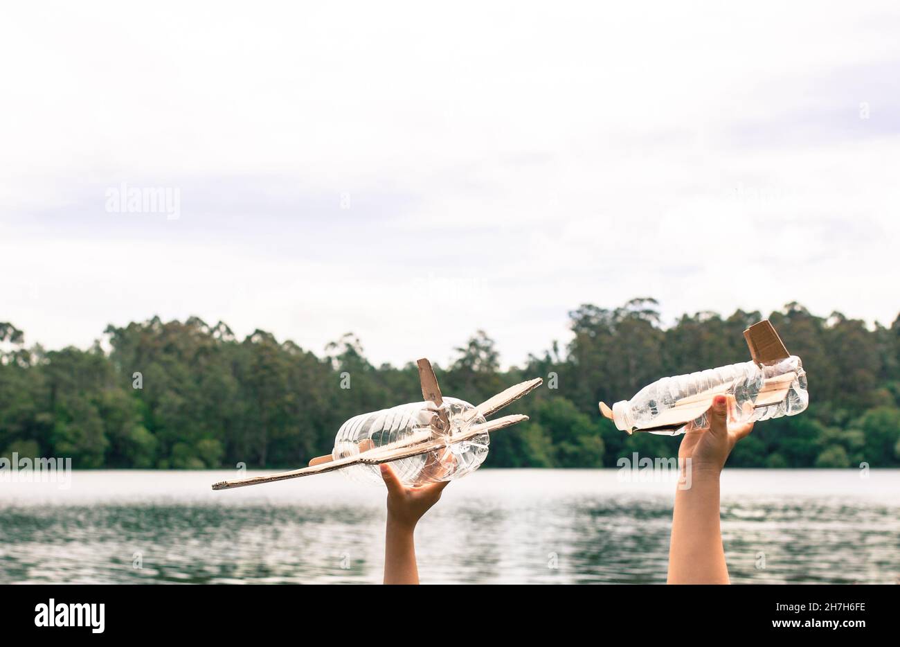 Kinderhände spielen mit einem Flugzeug aus recyceltem Material (Holz, PVC-Flaschen, Pappe) Stockfoto