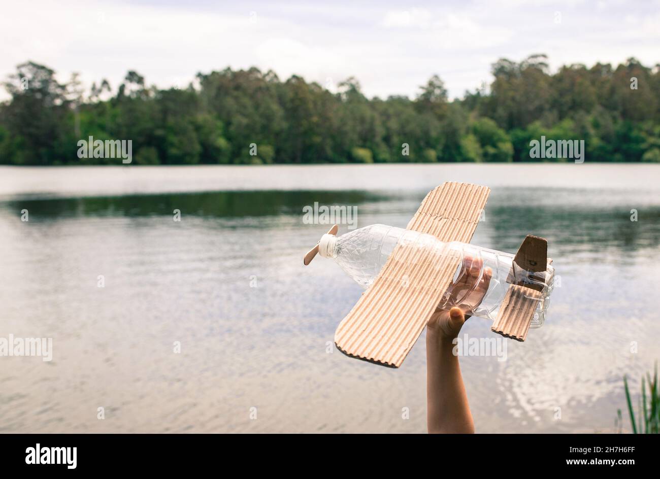 Kinderhände spielen mit einem Flugzeug aus recyceltem Material (Holz, PVC-Flaschen, Pappe) Stockfoto