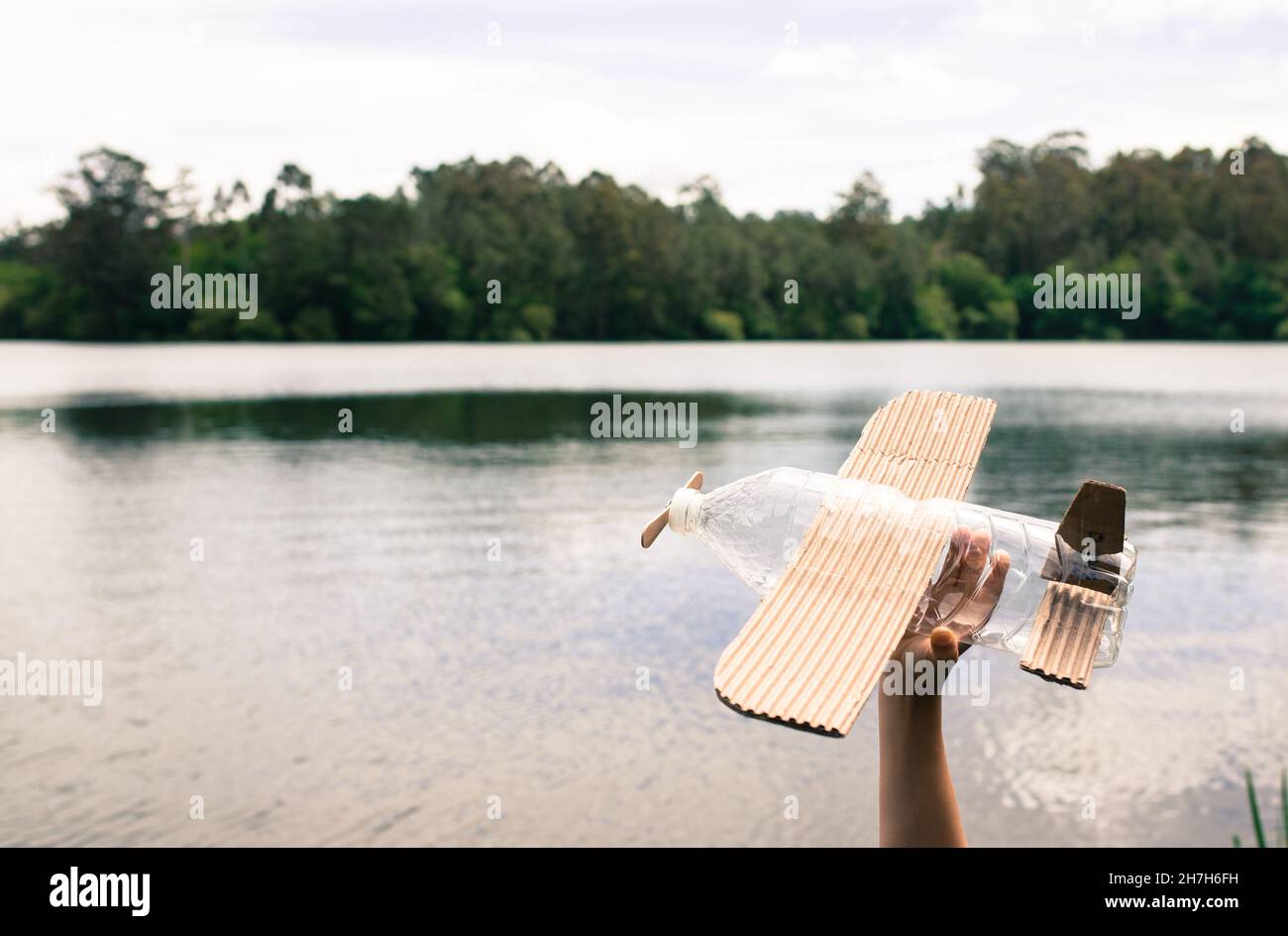 Kinderhände spielen mit einem Flugzeug aus recyceltem Material (Holz, PVC-Flaschen, Pappe) Stockfoto