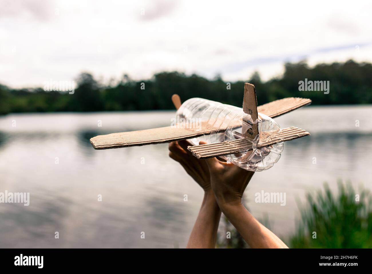 Kinderhände spielen mit einem Flugzeug aus recyceltem Material (Holz, PVC-Flaschen, Pappe) Stockfoto