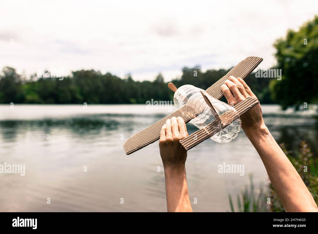 Kinderhände spielen mit einem Flugzeug aus recyceltem Material (Holz, PVC-Flaschen, Pappe) Stockfoto