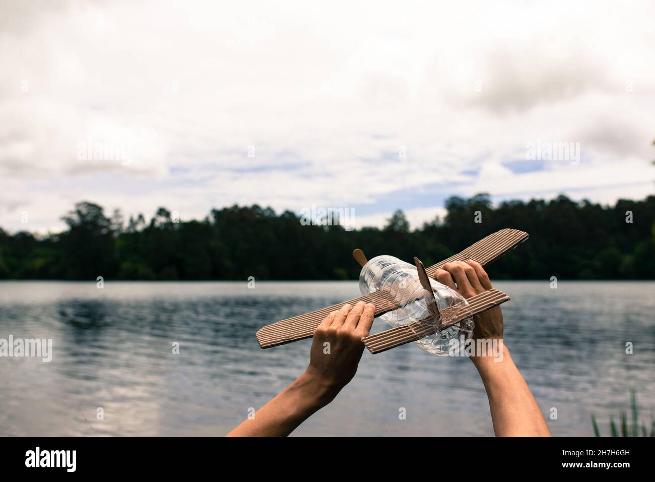 Kinderhände spielen mit einem Flugzeug aus recyceltem Material (Holz, PVC-Flaschen, Pappe) Stockfoto
