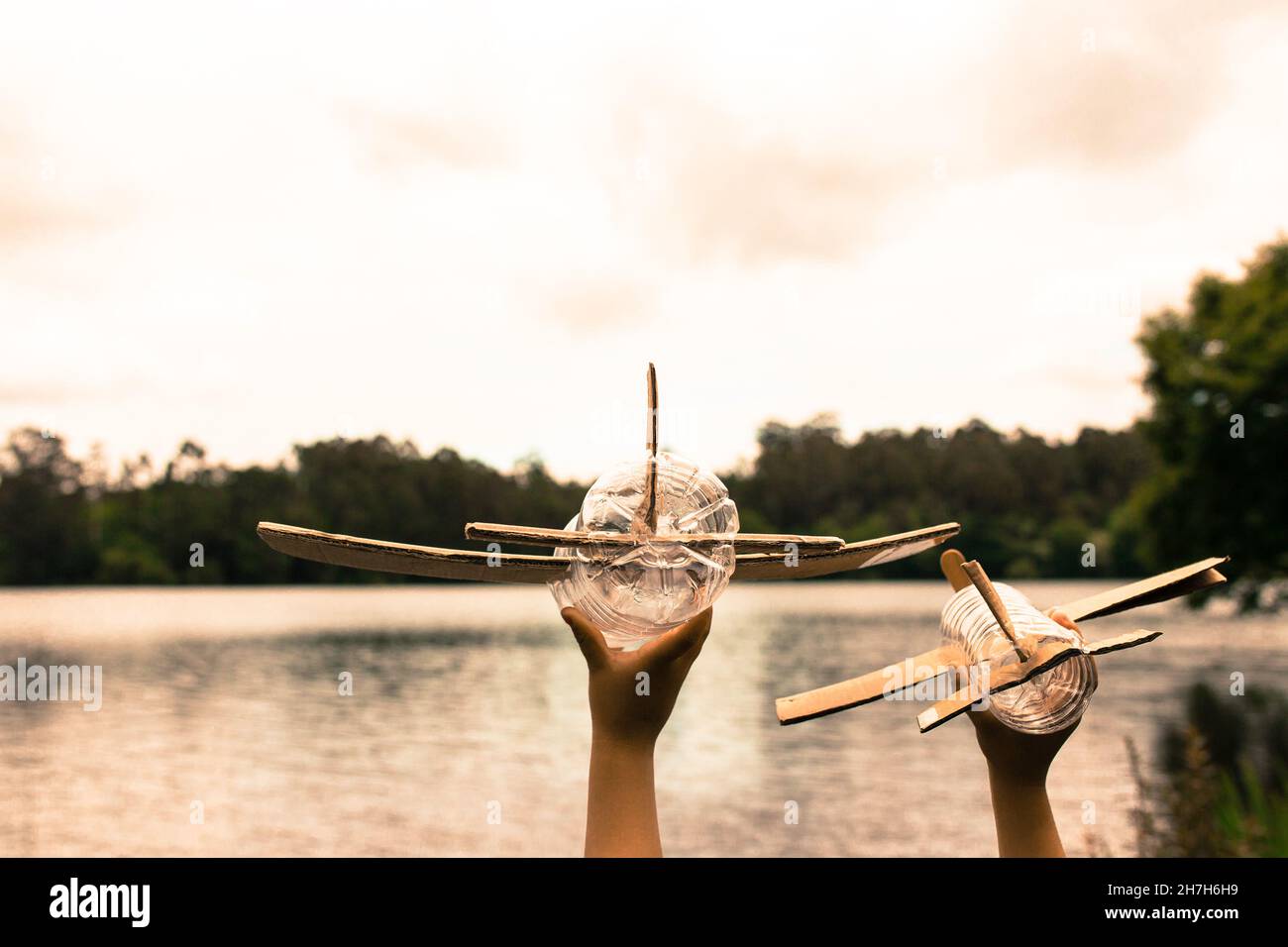 Kinderhände spielen mit einem Flugzeug aus recyceltem Material (Holz, PVC-Flaschen, Pappe) Stockfoto
