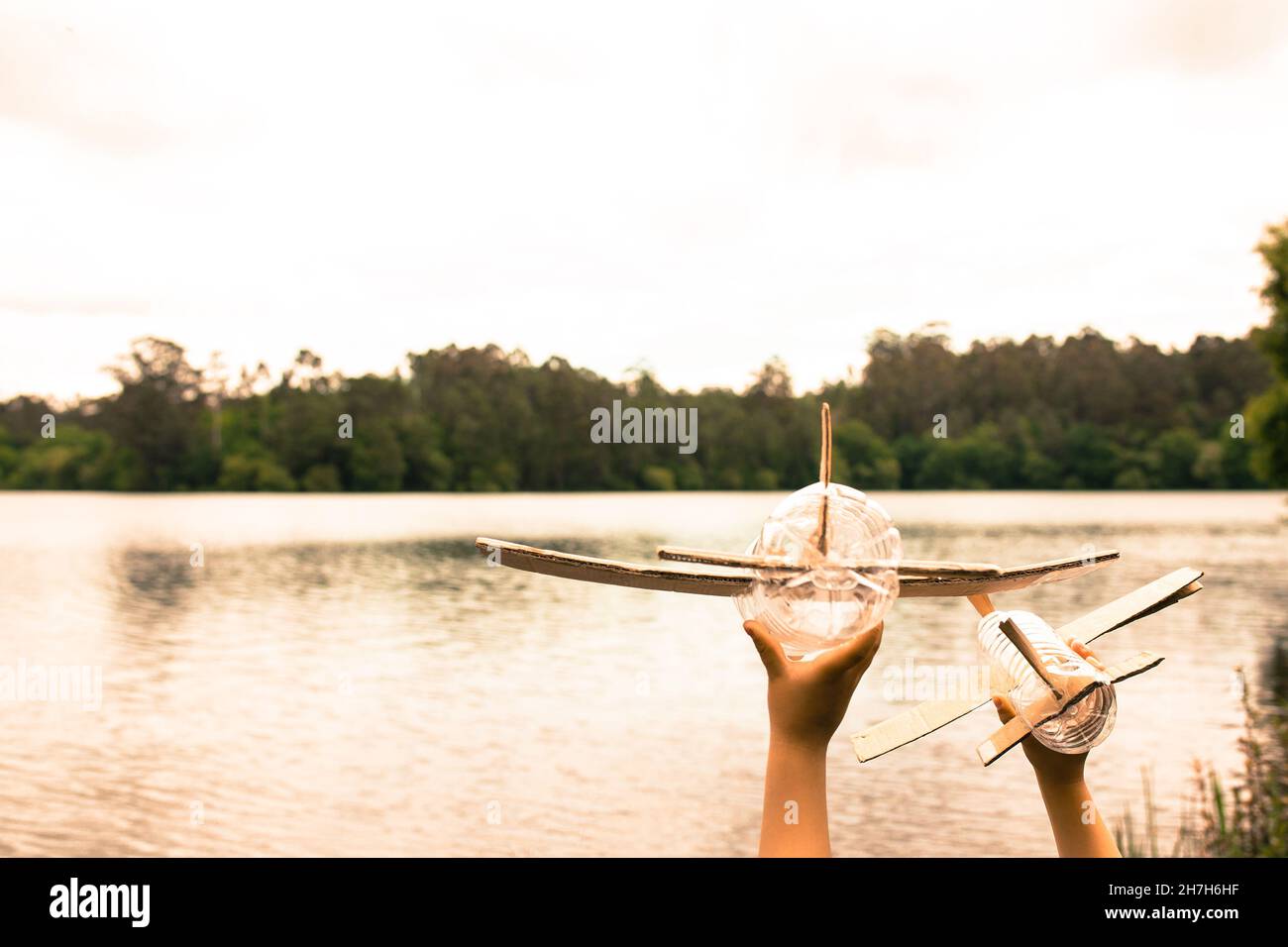 Kinderhände spielen mit einem Flugzeug aus recyceltem Material (Holz, PVC-Flaschen, Pappe) Stockfoto