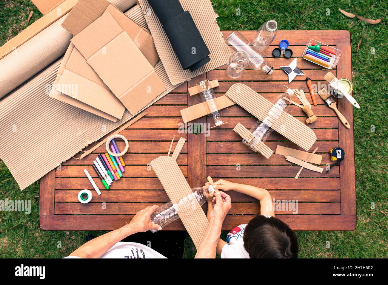 Großvater und Enkel bauen Flugzeuge aus recyceltem Material (Pappe, PVC-Flaschen, Holz). Arbeitsideen Kreislaufwirtschaft, Recycling, Umwelt Stockfoto