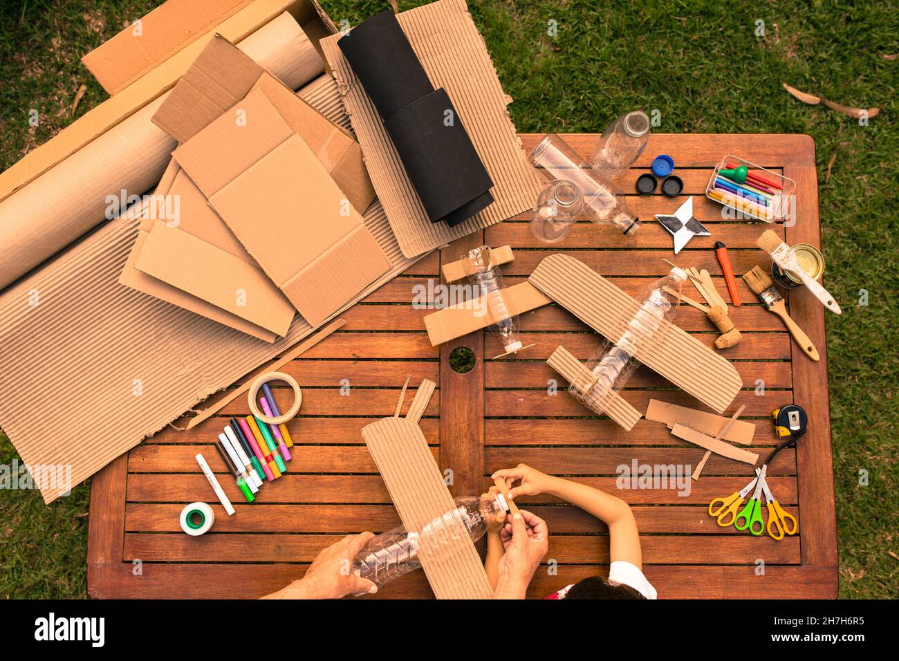 Großvater und Enkel bauen Flugzeuge aus recyceltem Material (Pappe, PVC-Flaschen, Holz). Arbeitsideen Kreislaufwirtschaft, Recycling, Umwelt Stockfoto