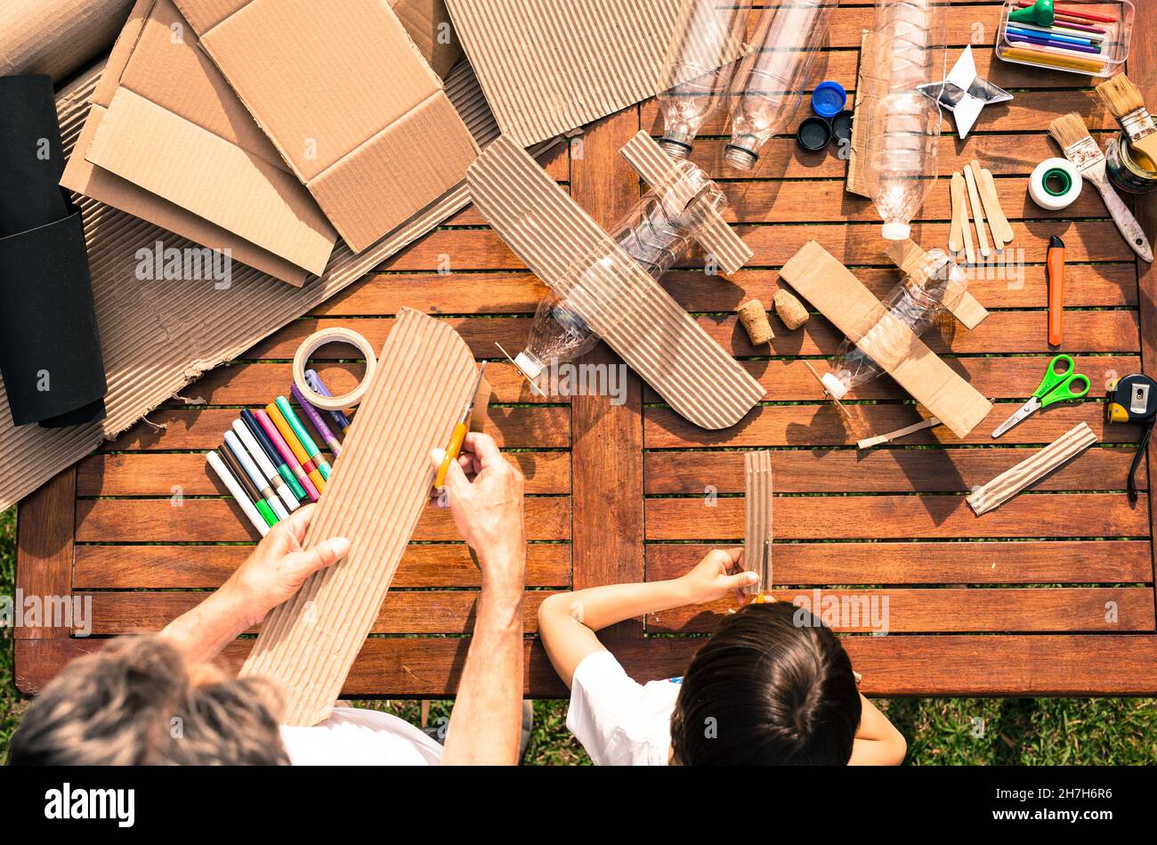 Großvater und Enkel bauen Flugzeuge aus recyceltem Material (Pappe, PVC-Flaschen, Holz). Arbeitsideen Kreislaufwirtschaft, Recycling, Umwelt Stockfoto