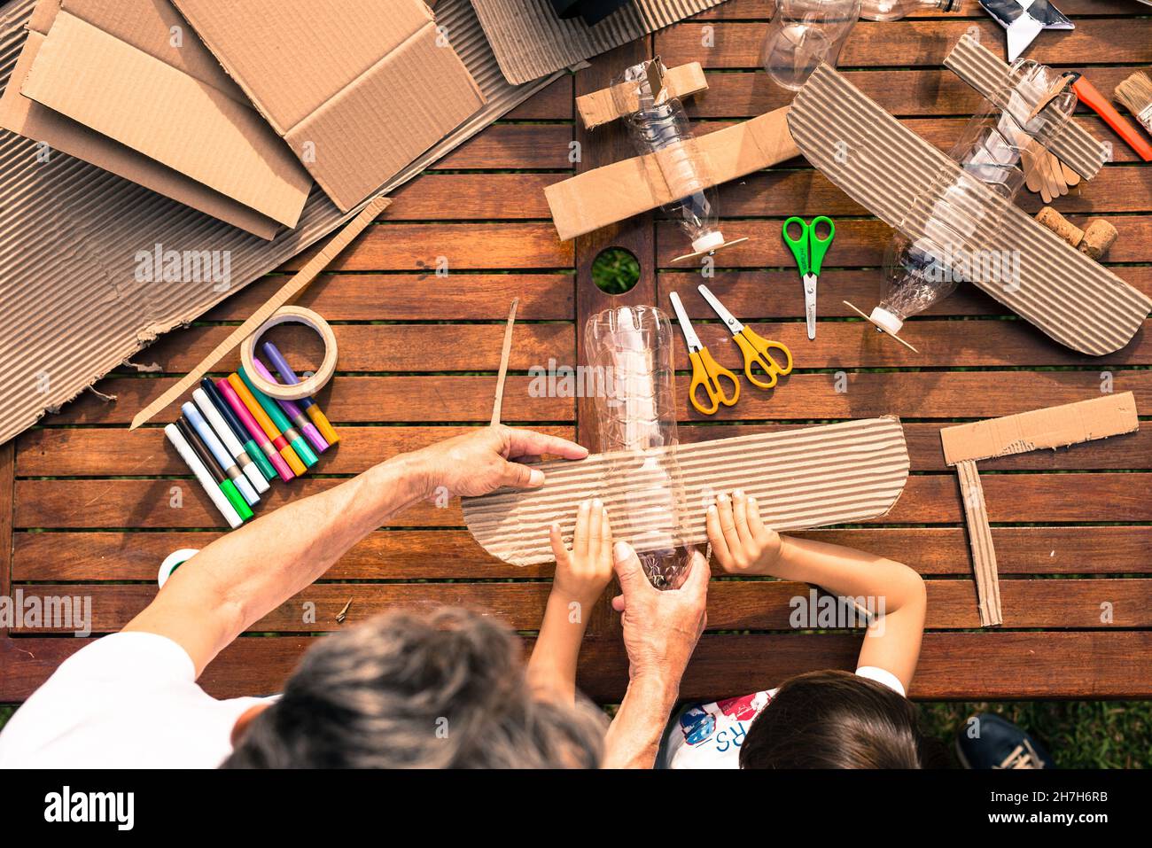 Großvater und Enkel bauen Flugzeuge aus recyceltem Material (Pappe, PVC-Flaschen, Holz). Arbeitsideen Kreislaufwirtschaft, Recycling, Umwelt Stockfoto