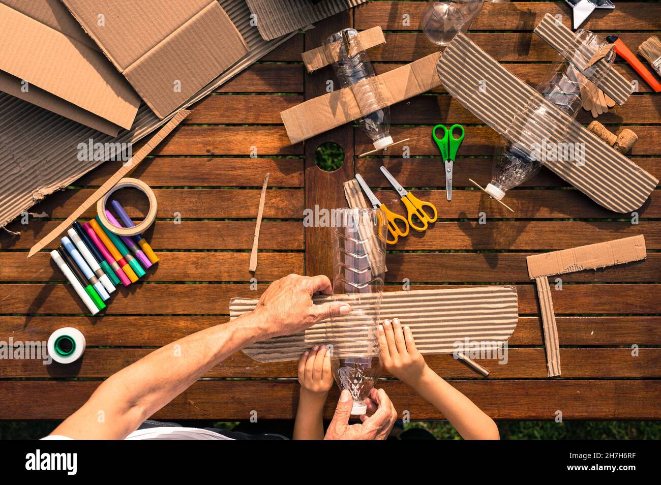 Großvater und Enkel bauen Flugzeuge aus recyceltem Material (Pappe, PVC-Flaschen, Holz). Arbeitsideen Kreislaufwirtschaft, Recycling, Umwelt Stockfoto