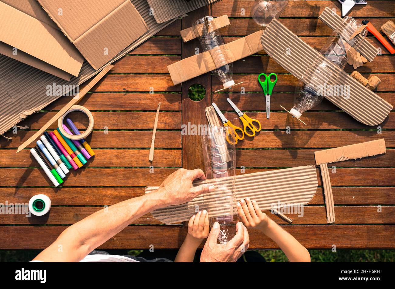 Großvater und Enkel bauen Flugzeuge aus recyceltem Material (Pappe, PVC-Flaschen, Holz). Arbeitsideen Kreislaufwirtschaft, Recycling, Umwelt Stockfoto