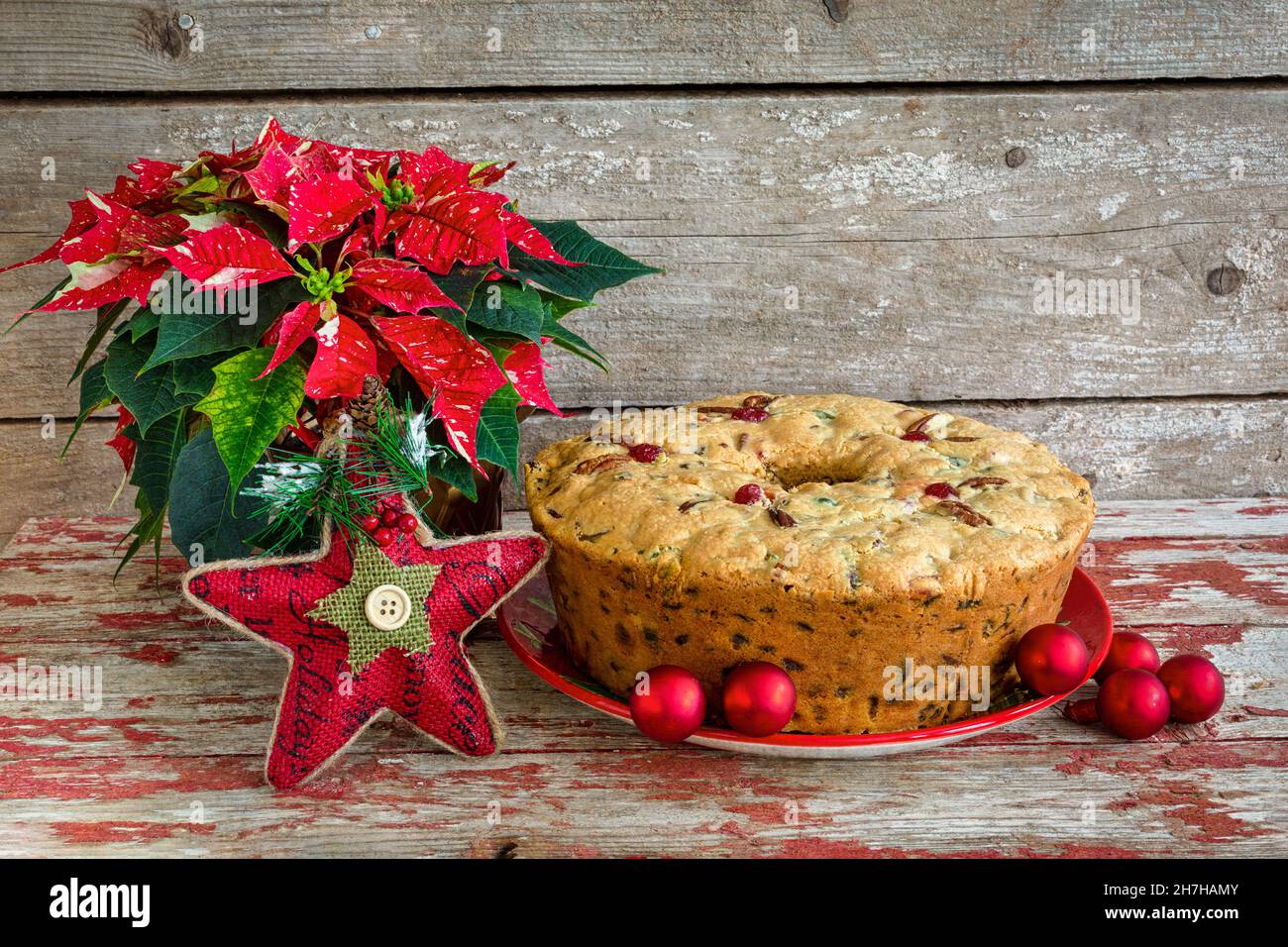 Traditioneller weihnachtlicher Obstkuchen mit Weihnachtsstern und Weihnachtsschmuck auf rustikalem Holzhintergrund. Stockfoto