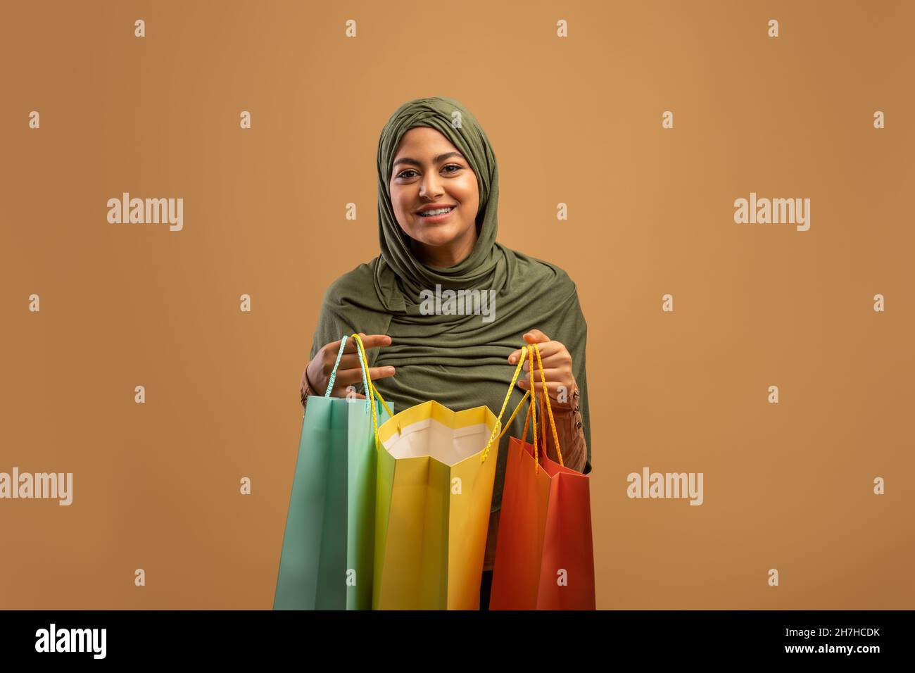 Zufriedener Kunde. Aufgeregte arabische Frau öffnet bunte Einkaufstaschen und lächelt an Kamera, brauner Hintergrund, Banner Stockfoto