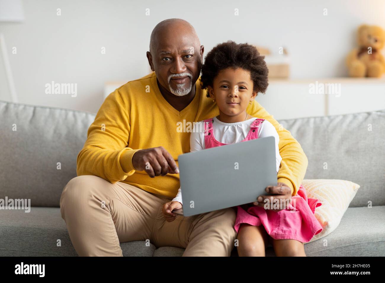 Fröhliches schwarzes kleines Kind und Opa im Internet surfen oder spielen ein Online-Spiel, sehen Cartoon auf Laptop Stockfoto