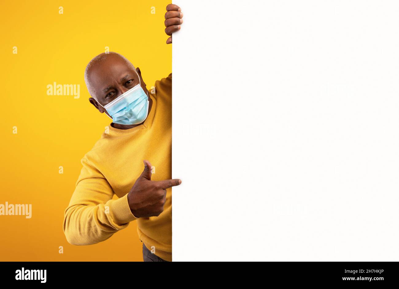 Älterer schwarzer Mann, der auf ein leeres Papierbanner zeigt, eine Anti-Covid-Maske trägt, für Ihr Produkt oder Ihre Dienstleistung wirbt, ein Modell Stockfoto