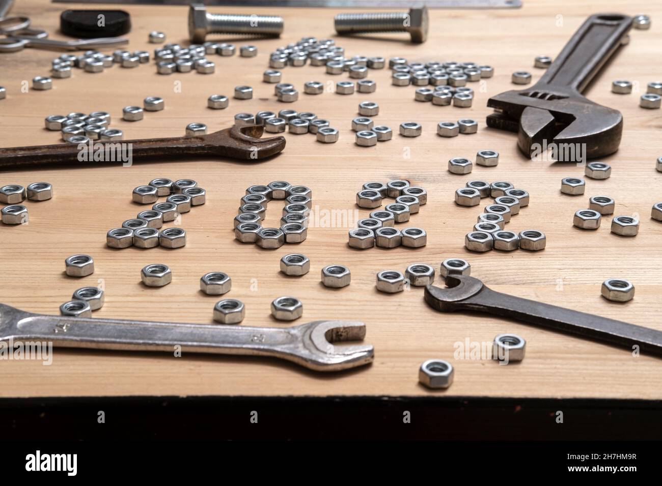 Die Nummer 2022 ist mit Metallmuttern auf einem Holztisch neben einer Vielzahl von Schraubenschlüsseln und Schrauben ausgekleidet. Konzept der Vorbereitung auf das neue Jahr. Stockfoto
