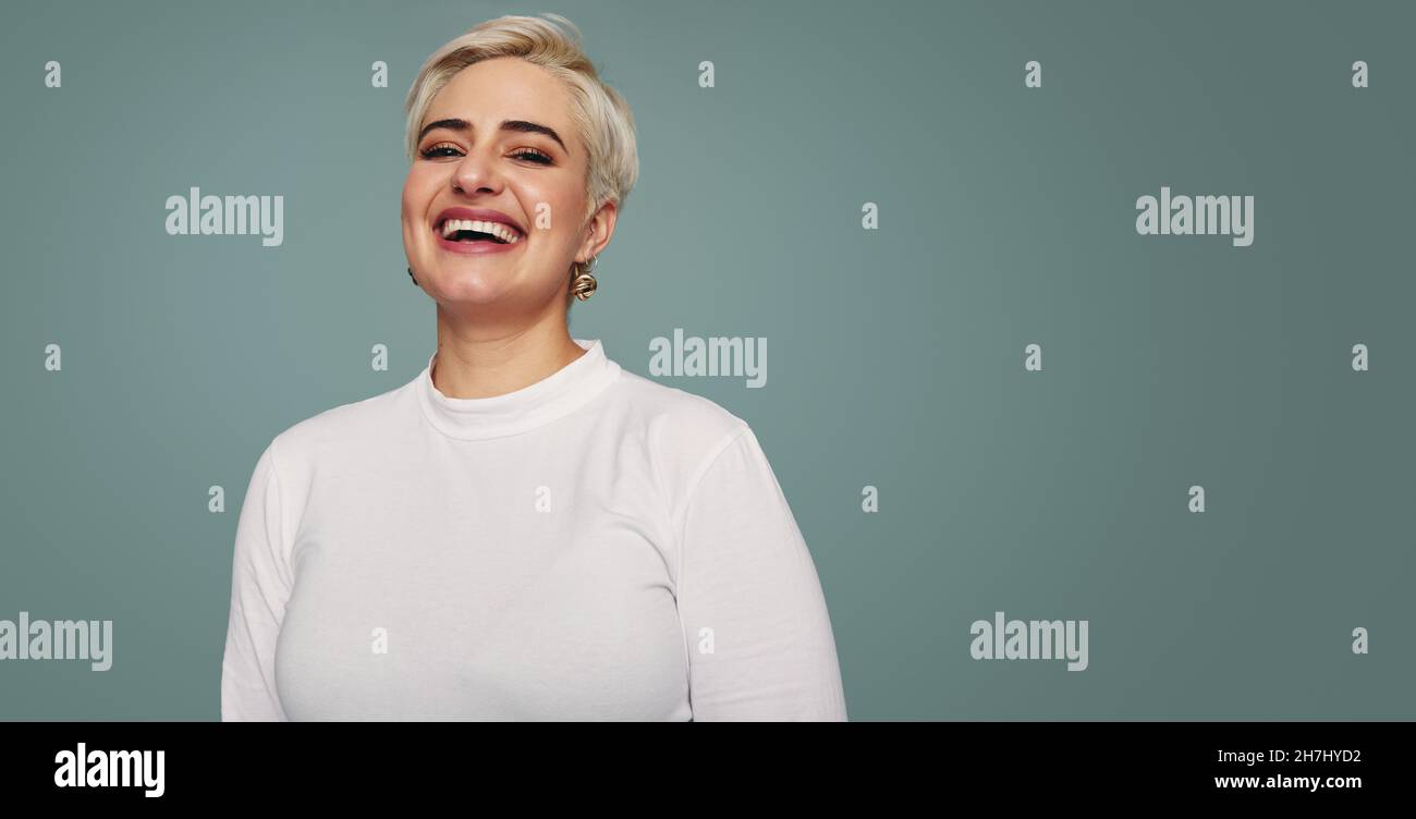 Lächelnde blonde Frau, die allein in einem Studio steht. Fröhliche Frau mittleren Erwachsenen, die fröhlich auf die Kamera schaut, während sie vor einem Studiohintergrund steht. Stockfoto