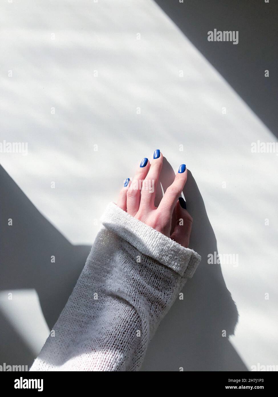 Hand mit blauen Nägeln auf dem weißen Tisch Stockfoto