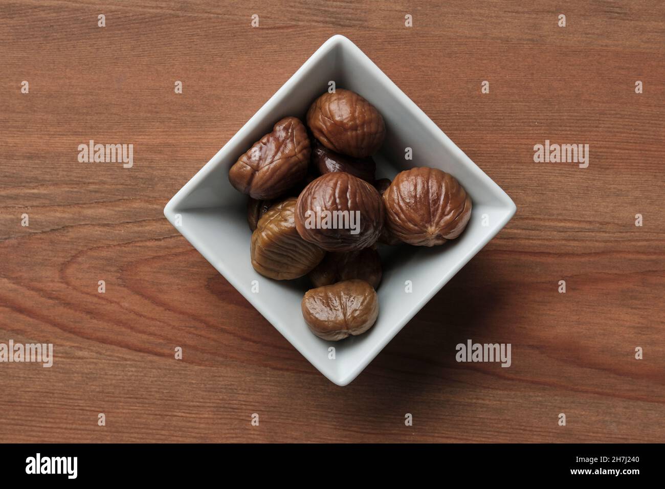 Quadratische Schüssel mit sechs gerösteten Kastanien auf einem Holztisch Stockfoto