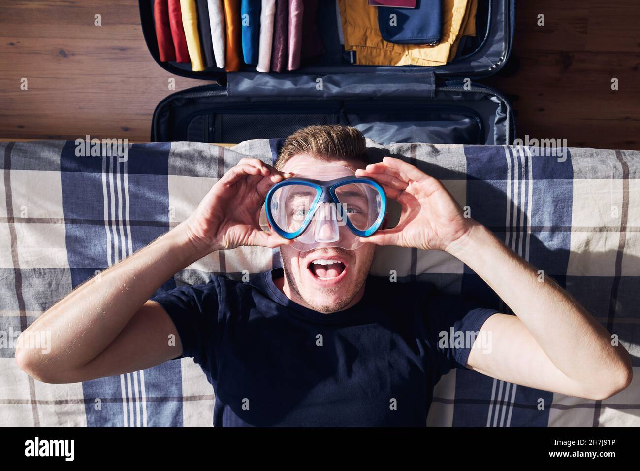 Verrücktes Porträt eines glücklichen jungen Mannes beim Packen von Koffern und der Planung von Reiseabenteuern. Stockfoto