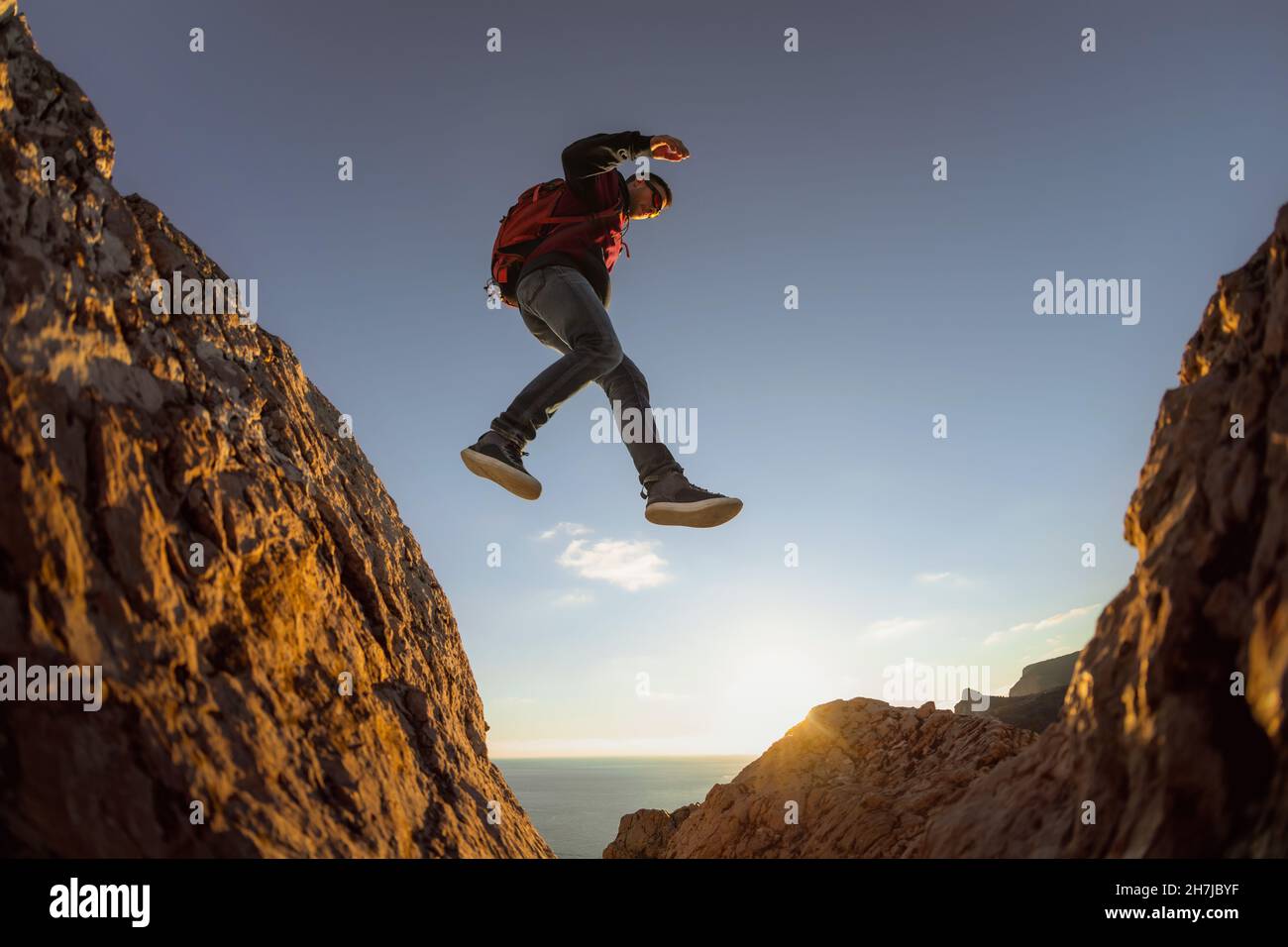 Sportlicher Wanderer mit Rucksack springt von Stein zu Stein gegen den blauen Himmel Stockfoto
