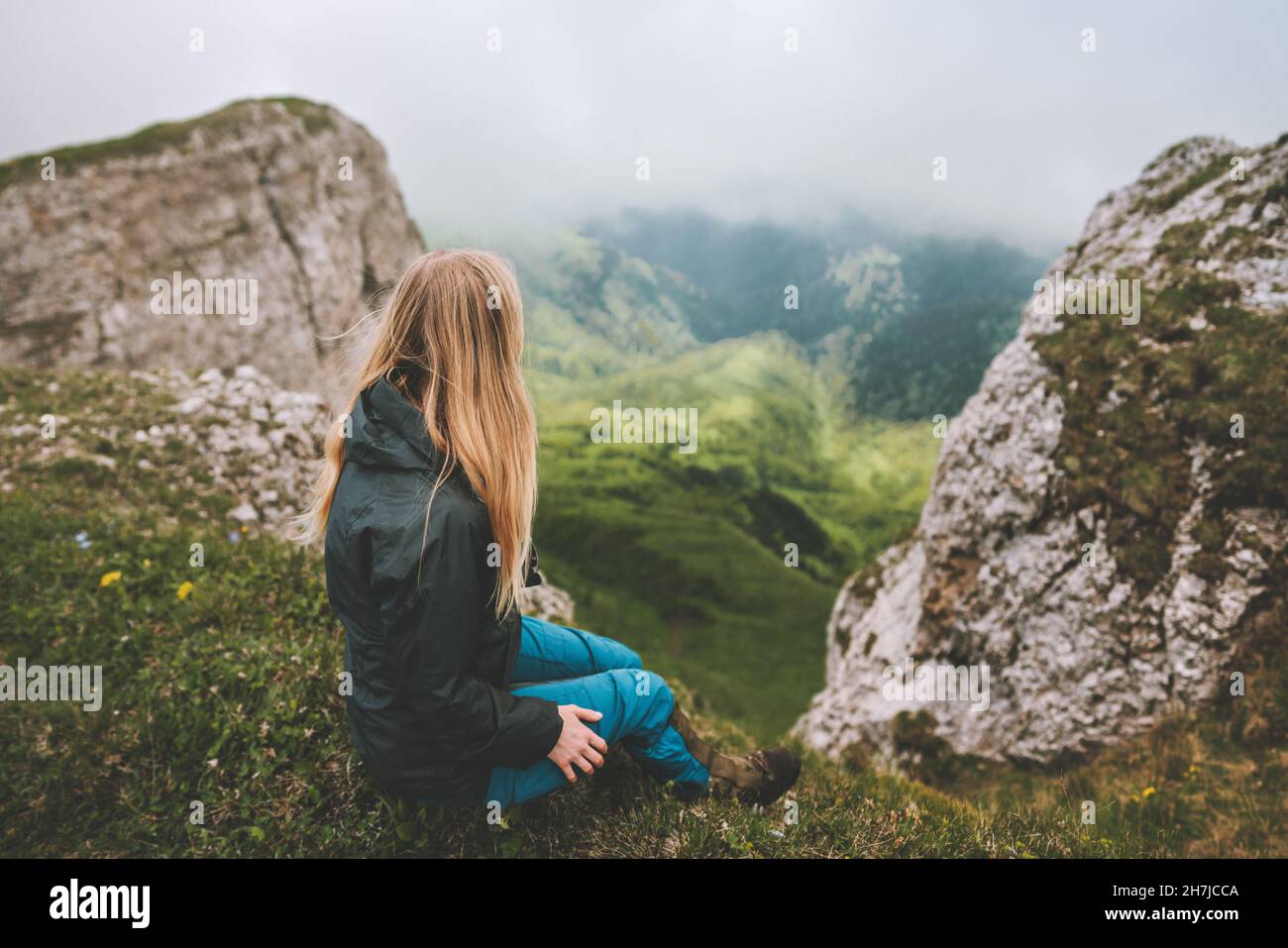 Frau, die alleine auf einer Klippe sitzt und die neblige Aussicht genießt, in den Bergen wandern, Abenteuer im Freien, Urlaub mit gesunder Lebensweise Stockfoto