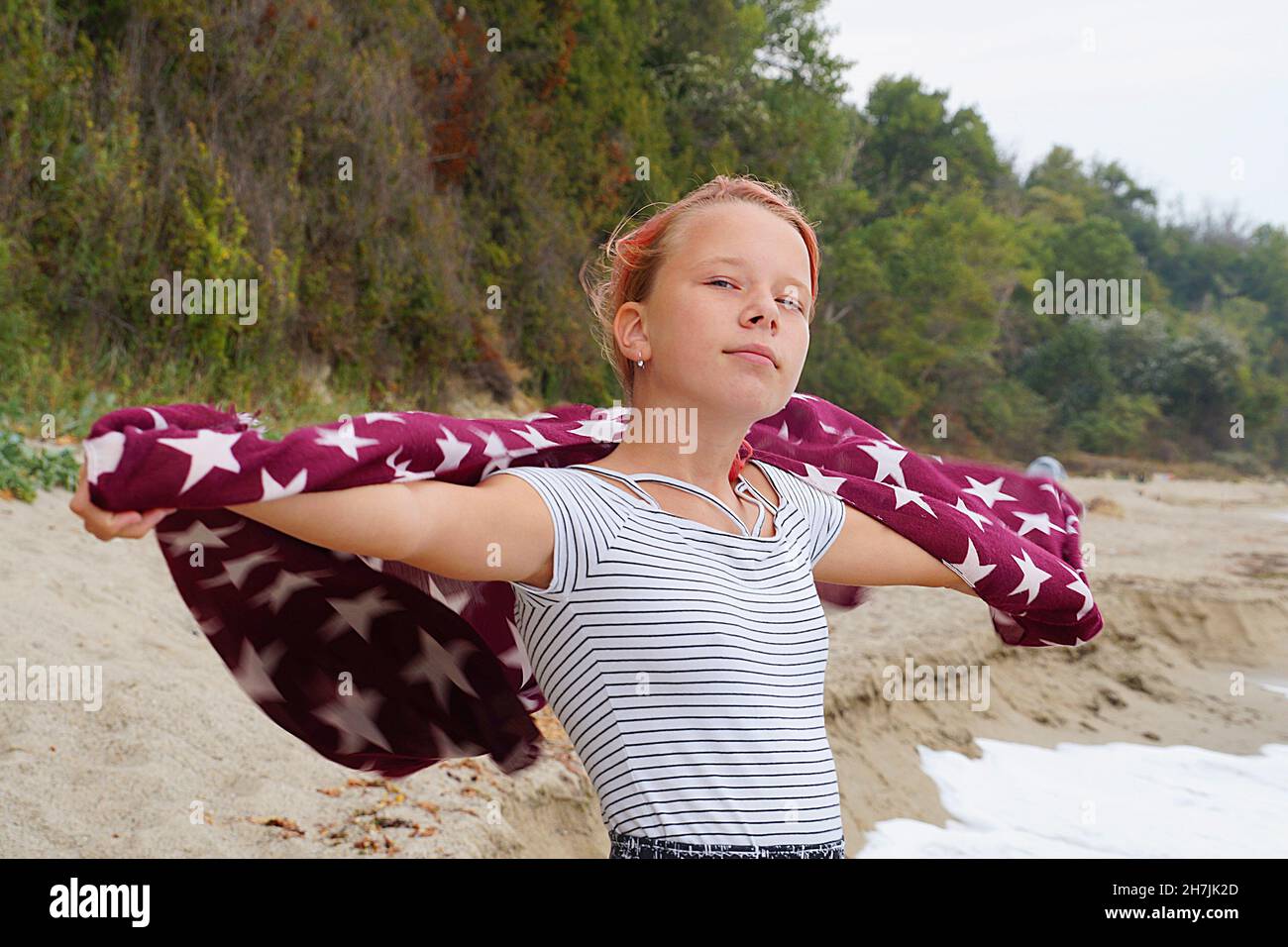 Teenager-Mädchen hält einen Schal im Wind mit ausgestreckten Händen an der Küste. Stockfoto