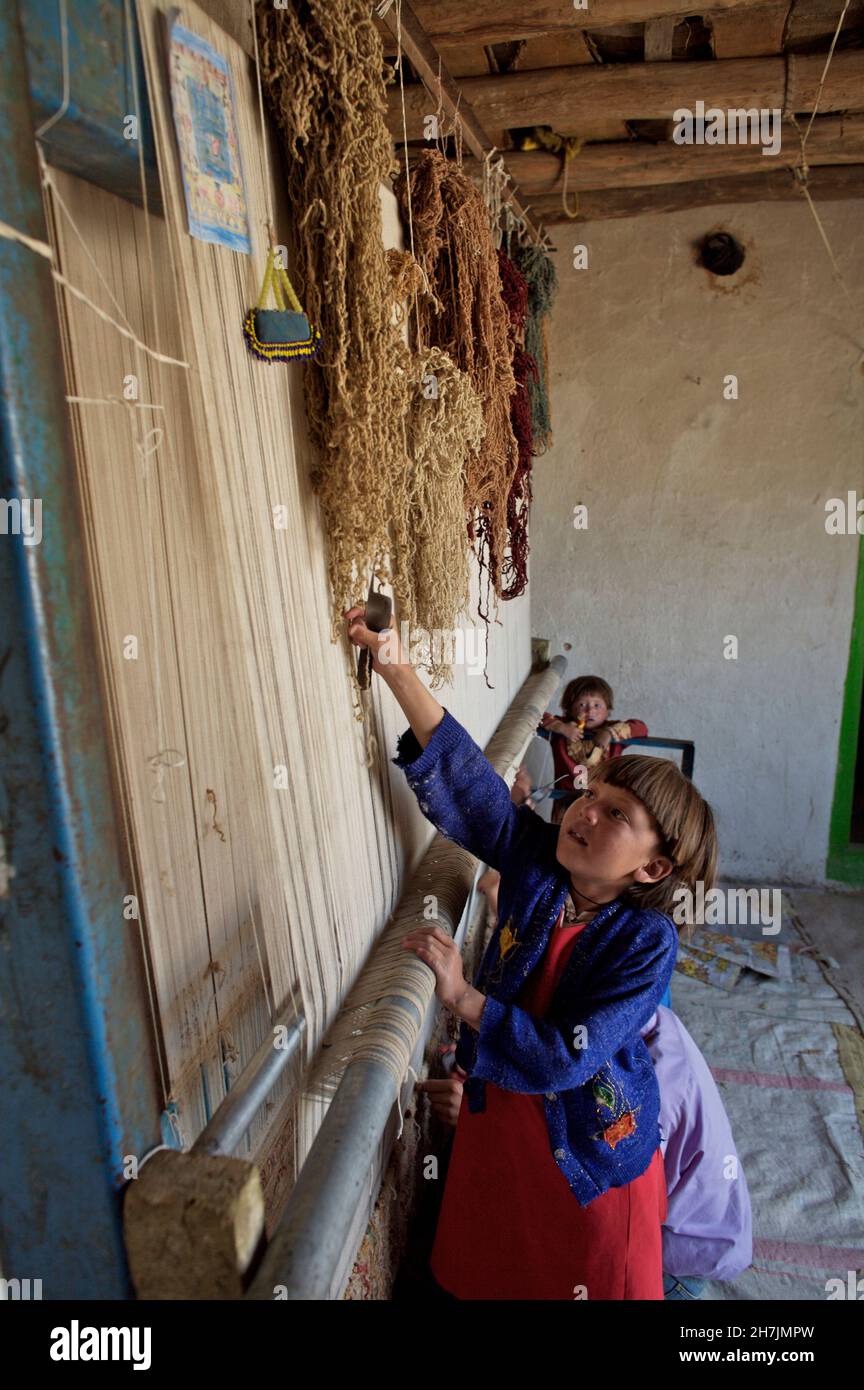 Ganz links - Aqila, 8, und ihre Brüder, die auf einem traditionellen Webstuhl einen Teppich weben, in ihrem Haus, im Dorf Ragshad, in der zentralen Bamyan-Provinz Stockfoto