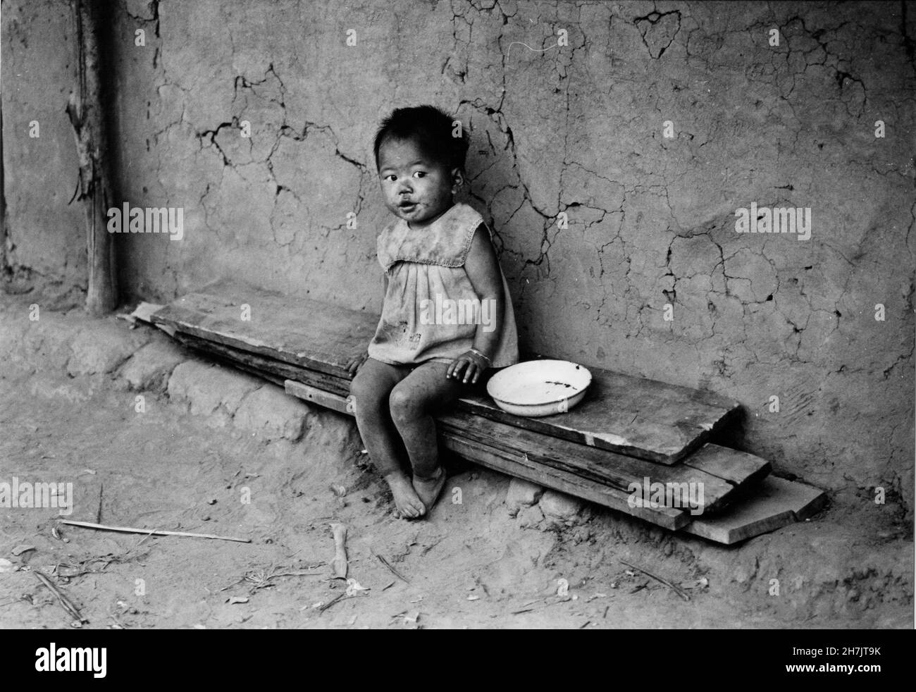 Ein junges Mädchen aus der ethnischen Minderheit der Chakma sitzt auf Holzbohlen vor ihrem Schlammhaus in Rangamati in der Region Chittagong Hill Tracts Stockfoto