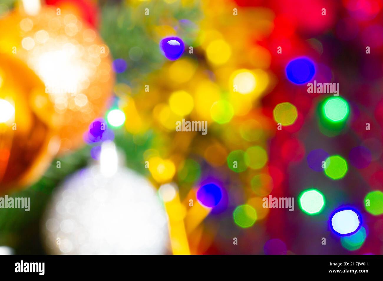 Weihnachtsspielzeug auf dem Weihnachtsbaum auf dem bunten Lichthintergrund. Wunderschöne Weihnachtsdekorationen aus Glas. Coole helle Neujahrsspielzeuge Stockfoto