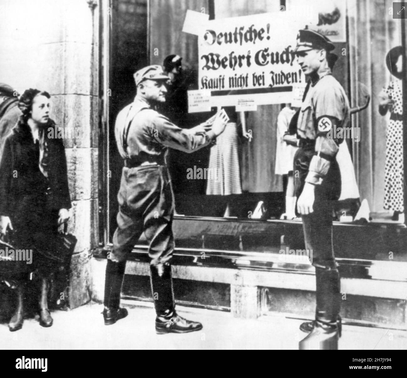 KRISTALLNACHT ein SS-Soldat, der im November 1938 eine Nachricht an das Fenster eines Ladens in der Friedrichstraße in Berlin postete. Er sagte den Deutschen, dass sie keine jüdischen Waren kaufen sollten. Der Mann rechts scheint einen Keulenfuß zu haben. Stockfoto