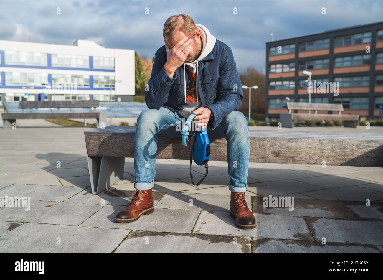 Zerbrochen mit Trauermann als Hundebesitzer trauert er, sitzt auf einer Bank mit dem schönen Halsband und der Leine und weint tief über Tierverluste Stockfoto