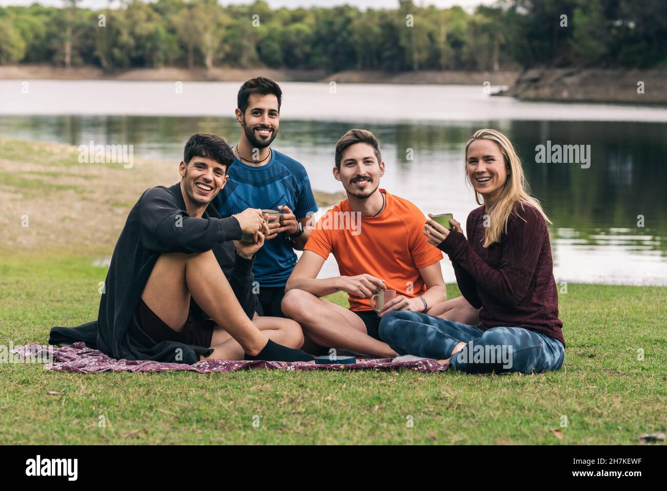Sportive Menschen, die der Kamera gegenüberstehen, während sie auf einem Park Tee trinken Stockfoto