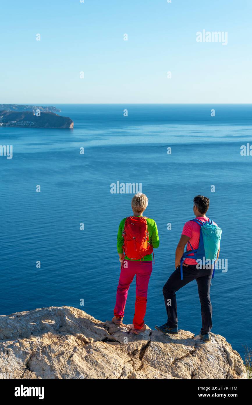 Zwei Wanderer stehen auf dem Gipfel über dem mittelmeer und den Hügeln und blicken auf Calpe, Provinz Alicante, Spanien Stockfoto