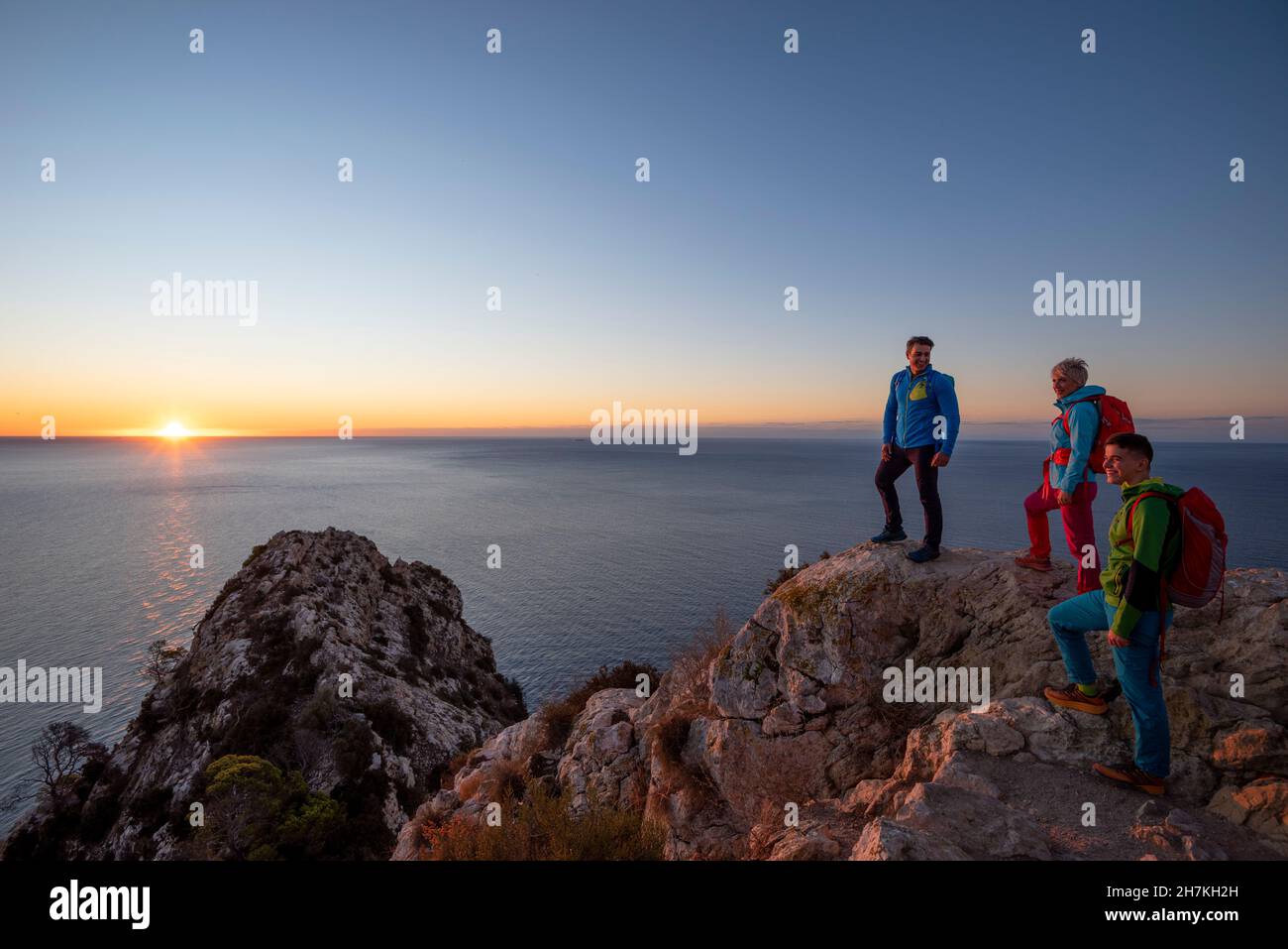 Drei Wanderer stehen auf dem Gipfel über dem mittelmeer und den Hügeln und blicken auf Calpe, Provinz Alicante, Spanien Stockfoto