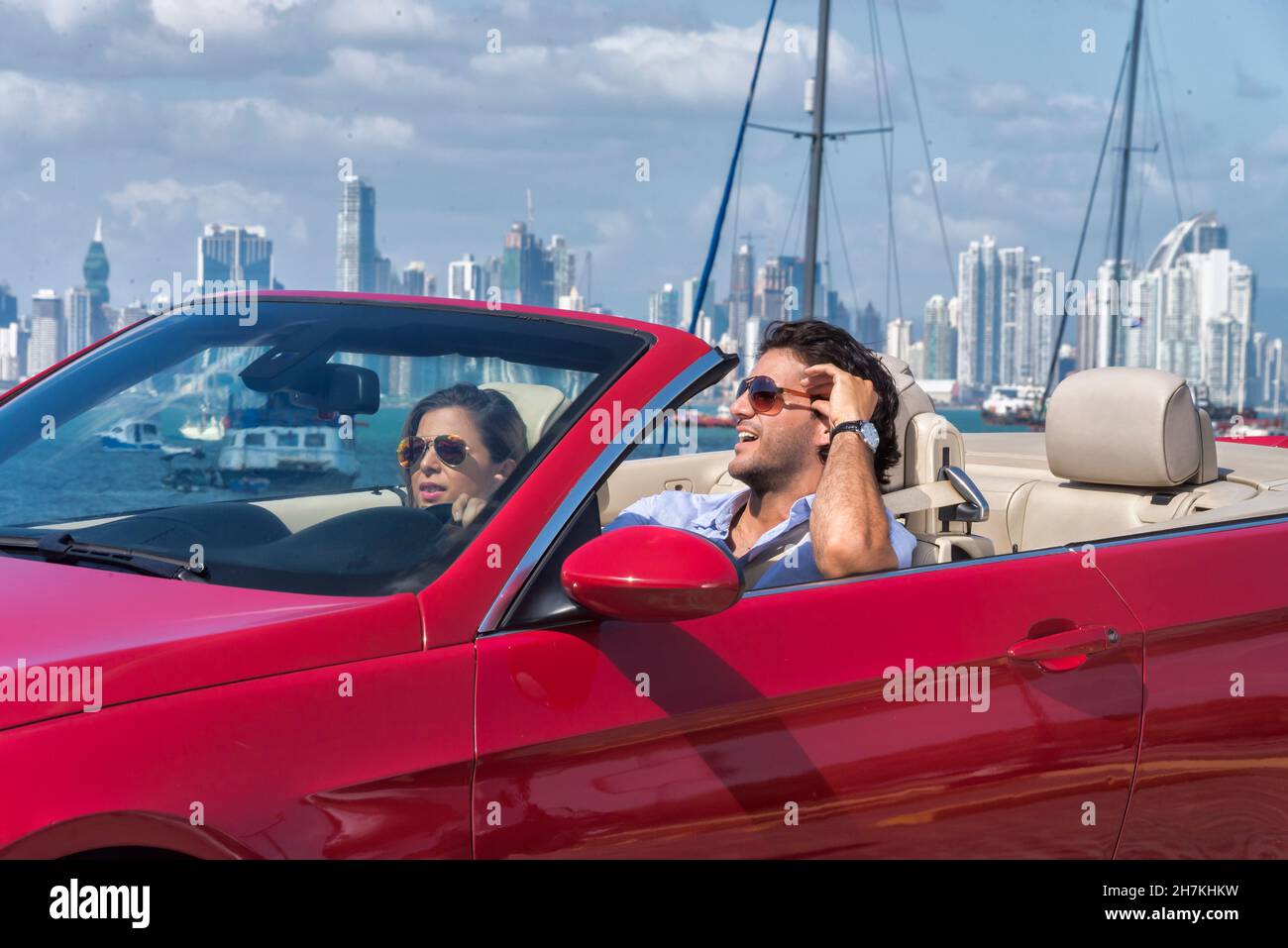 Lateinisches Paar, das lächelnd auf einem roten Cabrio mit panama City im Hintergrund reist Stockfoto