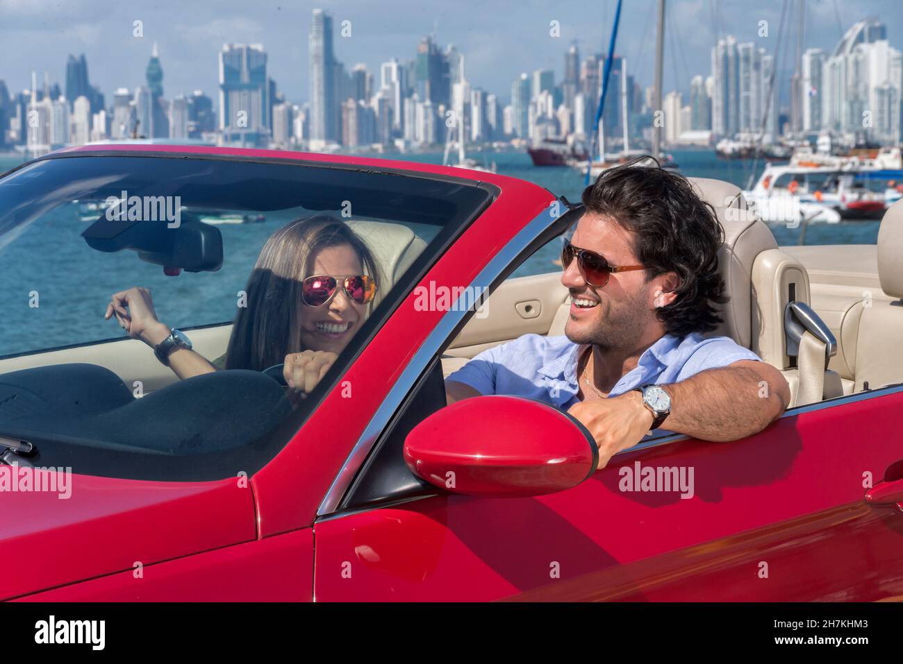 Glückliches lateinisches Paar, das auf einem roten Cabrio mit panama City im Hintergrund unterwegs ist Stockfoto
