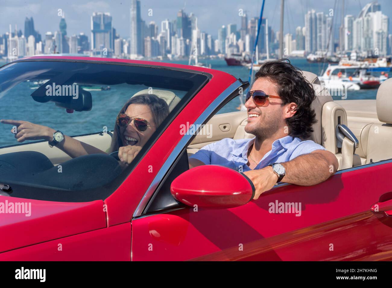 Lateinisches Paar, das auf einem roten Cabrio lachend mit panama City im Hintergrund reist Stockfoto