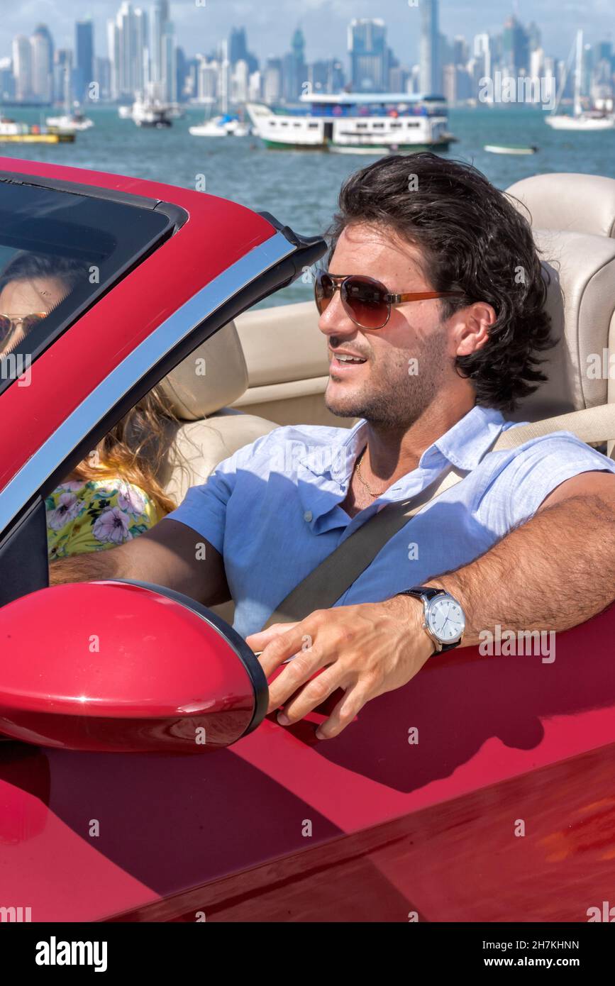 Glückliches lateinisches Paar, das auf einem roten Cabrio mit panama City im Hintergrund fährt Stockfoto