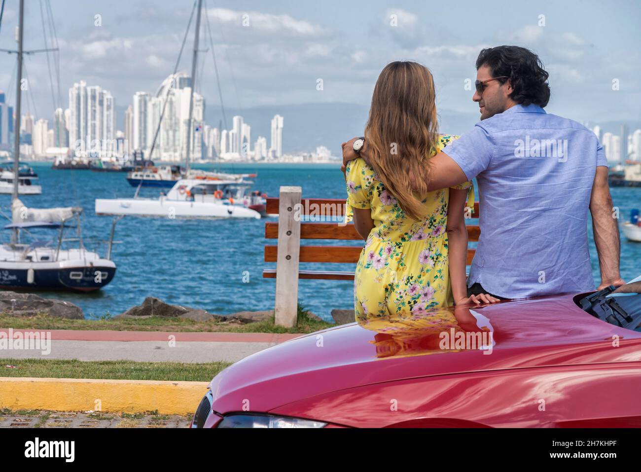 Ein lateinisches Paar lehnte sich an der Seite eines roten Autos und beobachtete Panama City Stockfoto