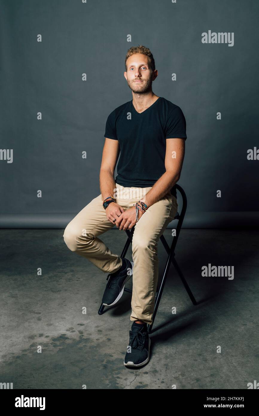 Mann in legerer Kleidung sitzt auf einem Stuhl vor grauem Hintergrund Stockfoto