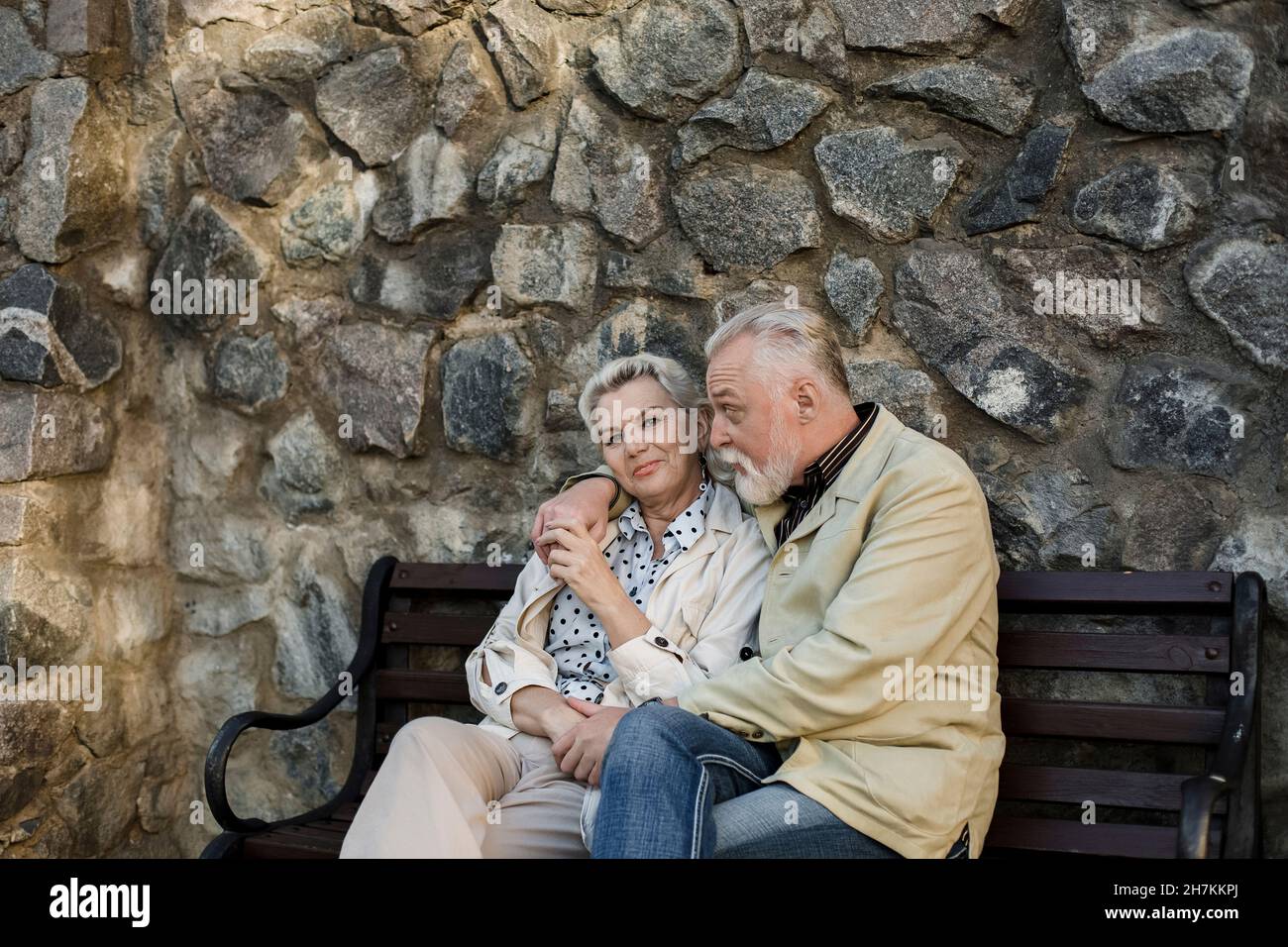 Mann mit Frau, die auf einer Bank vor einer Steinmauer sitzt Stockfoto